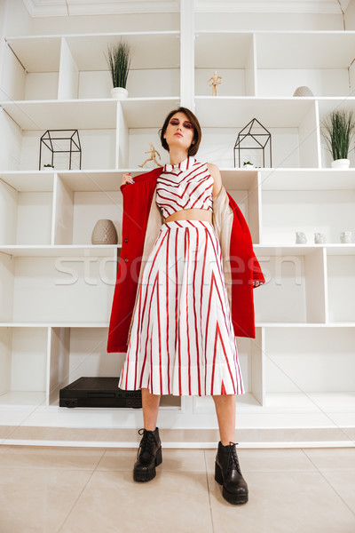 Beautiful young woman standing and taking off her red coat Stock photo © deandrobot