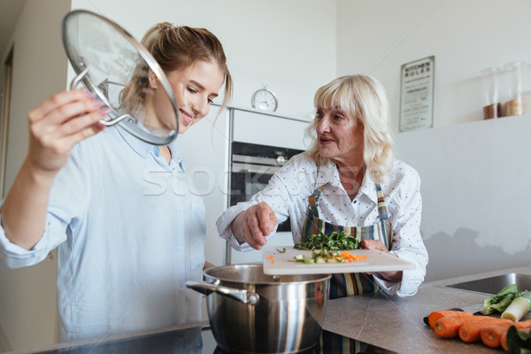 Cheerful young lady at home cooking in kitchen with grandmother Stock photo © deandrobot