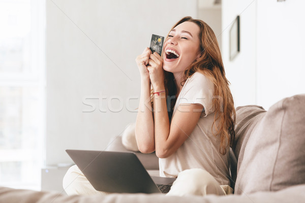 Happy woman with credit card and laptop sitting on sofa Stock photo © deandrobot