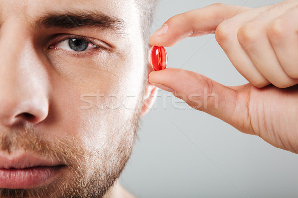 Close up portrait of a concentrated man holding red capsule Stock photo © deandrobot