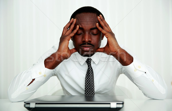 Pensive african businessman sitting at his workplace in office Stock photo © deandrobot