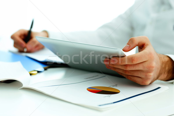 Closeup image of a man holding tablet computer and writing something down Stock photo © deandrobot