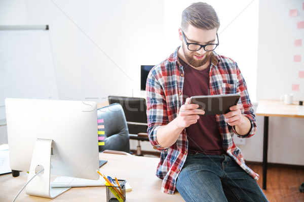 Smiling bearded man sitting with tablet on table in office Stock photo © deandrobot