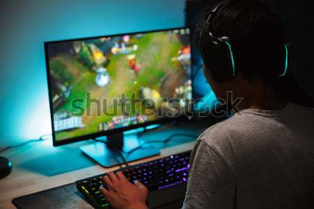 Concentrated gamer in headphones using computer for playing game  Stock photo © deandrobot