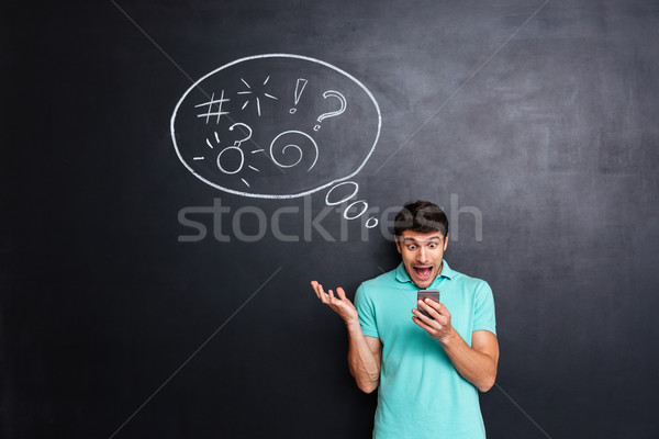 Crazy hysterical man using smartphone and screaming over chalkboard background Stock photo © deandrobot