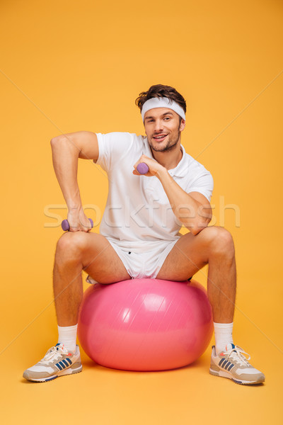 Smiling sportsman sitting on the fitness ball holding dumbbells Stock photo © deandrobot