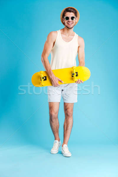Cheerful young man in hat and sunglasses holding skateboard Stock photo © deandrobot