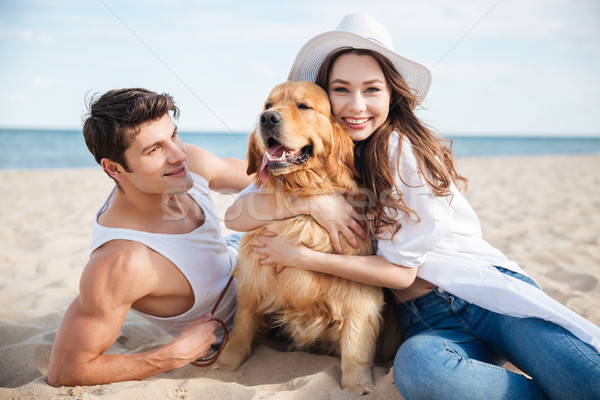 Smiling couple in love sitting on the beach with dog Stock photo © deandrobot