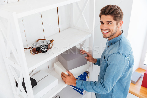 Smiling young man putting boxes on the shelves Stock photo © deandrobot