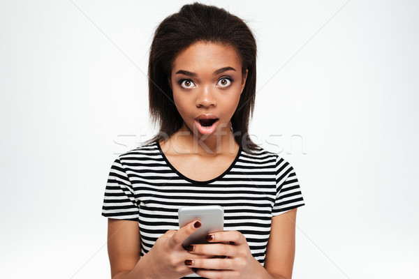 Shocked young african lady chatting by phone. Stock photo © deandrobot