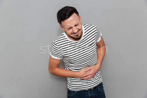 Displeased young man with painful feelings holding belly Stock photo © deandrobot