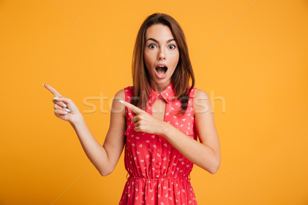Shocked brunette woman in dress winks and pointing up Stock photo © deandrobot