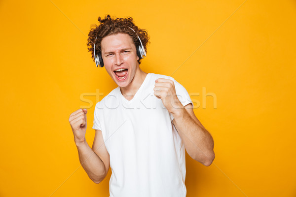 Stock photo: Photo of brunette joyous guy with curly hair listening to music 