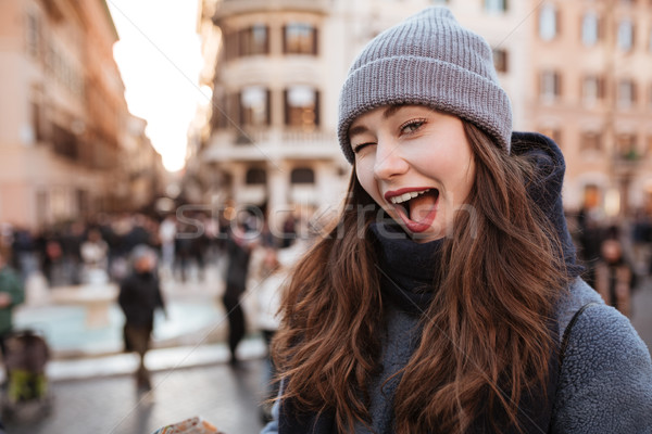 Cheerful woman standing and winking in the city Stock photo © deandrobot