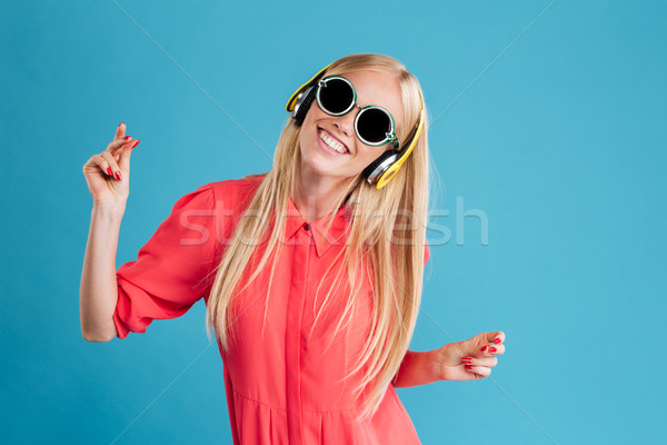 Cheerful woman in sunglasses listening music with headphones and dancing Stock photo © deandrobot