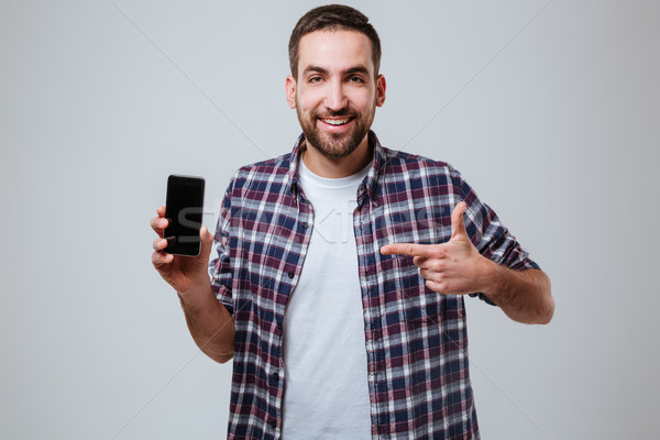 Bearded man showing blank smartphone screen and pointing at him Stock photo © deandrobot