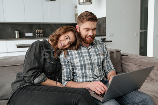 Happy loving couple lies on sofa using laptop computer. Stock photo © deandrobot