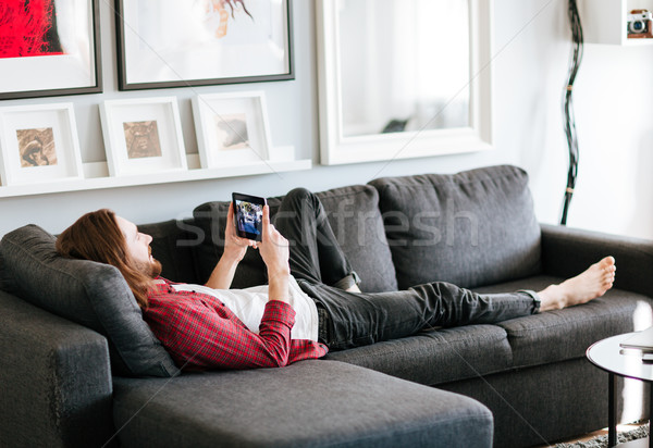 Stock photo: Relaxed man lying on sofa and watching video at home