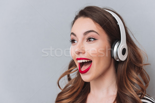 Happy young lady standing over grey wall and listening music Stock photo © deandrobot
