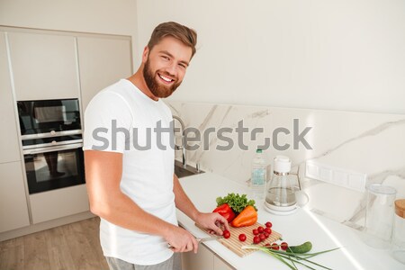 Side view of smiling bearded man cuts vegetables on kitchen Stock photo © deandrobot