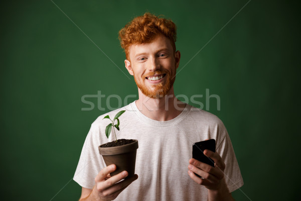 Stock photo: Portrait of young smiling redhead bearded young man, holding spo