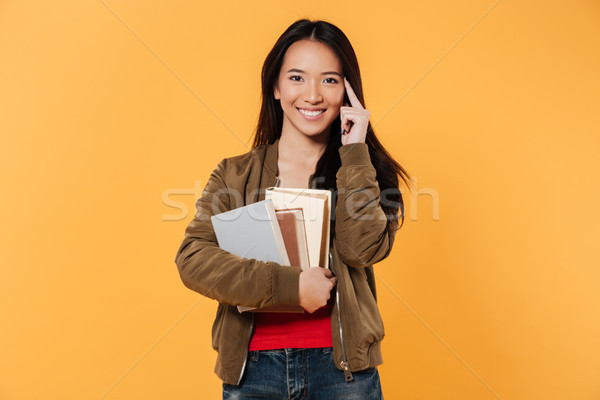 Smiling woman in jacket holding books while looking at camera Stock photo © deandrobot