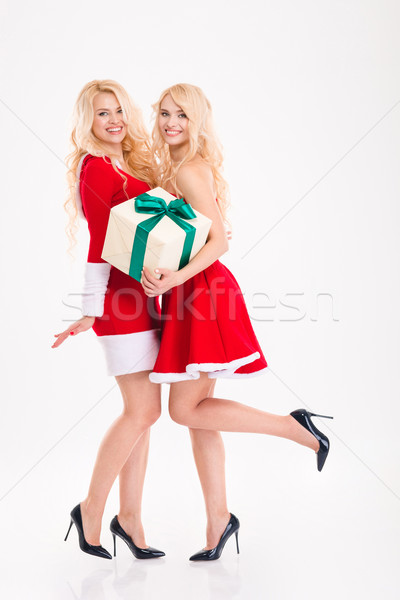 Two sisters twins in santa claus dresses holding one present  Stock photo © deandrobot