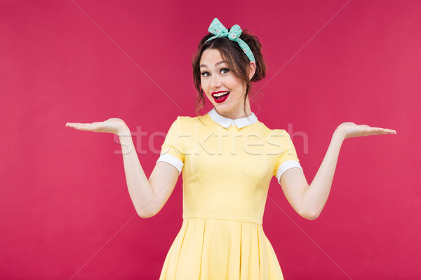 Smiling pinup girl in yellow dress holding copyspace on palms Stock photo © deandrobot