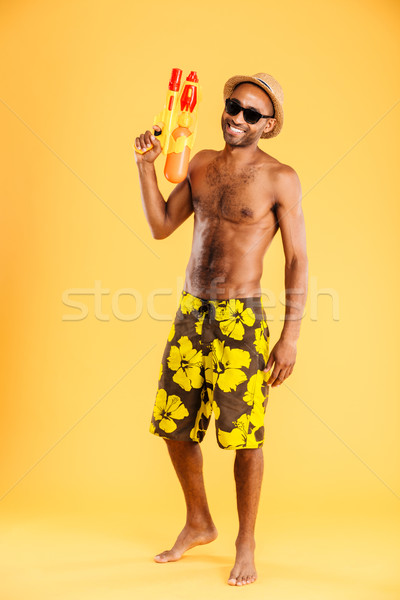 Full length of african man in swimwear holding water gun Stock photo © deandrobot