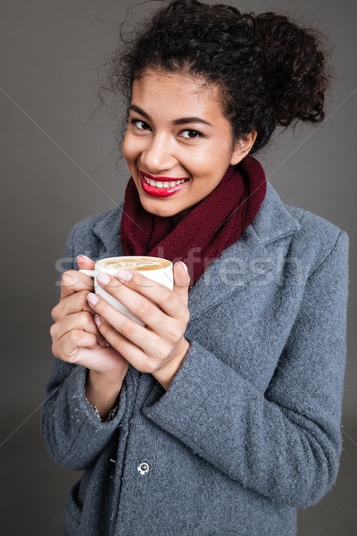 Smiling happy african woman in coat holding cup of coffee Stock photo © deandrobot