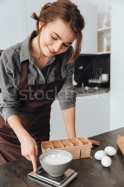 Happy woman standing in kitchen and cooking Stock photo © deandrobot