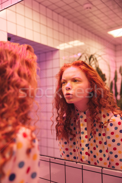 Concentrated young redhead curly lady looking at mirror. Stock photo © deandrobot