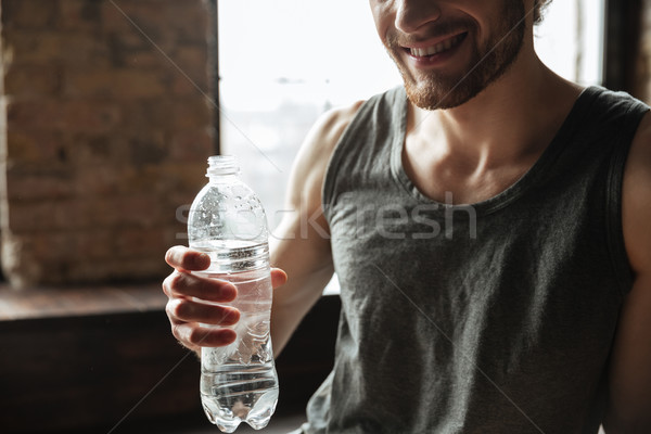 Cropped image of a smiling fitness man holding water bottle Stock photo © deandrobot