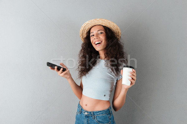Happy woman in hat holding smartphone and cup of coffee Stock photo © deandrobot