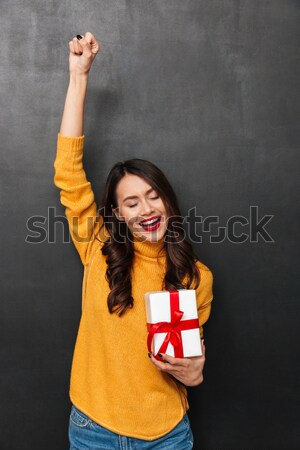 Smiling intrigued brunette woman in sweater holding gift box Stock photo © deandrobot