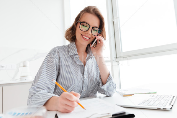 Beautiful smiling girl in glasses talking on mobile phone while  Stock photo © deandrobot