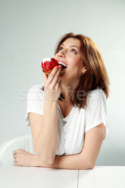Stock photo: Woman eating fresh strawberry cake and looking up  on gray background