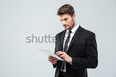 Concentrated young businessman standing and using tabet Stock photo © deandrobot