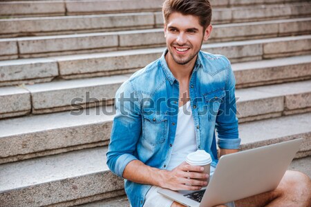Man drinking take away coffee and holding laptop while sitting Stock photo © deandrobot