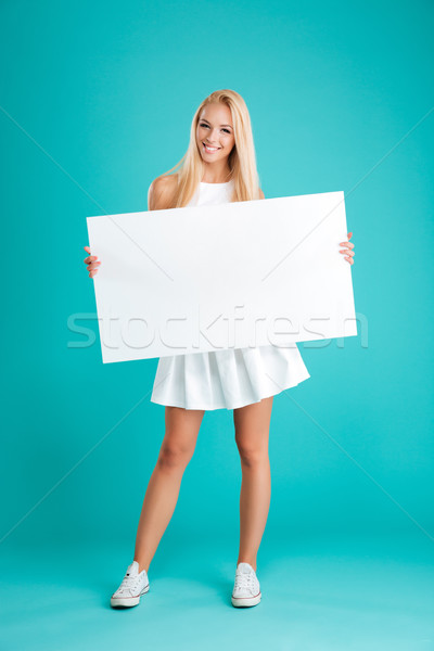 Smiling young woman standing and holding blank board Stock photo © deandrobot
