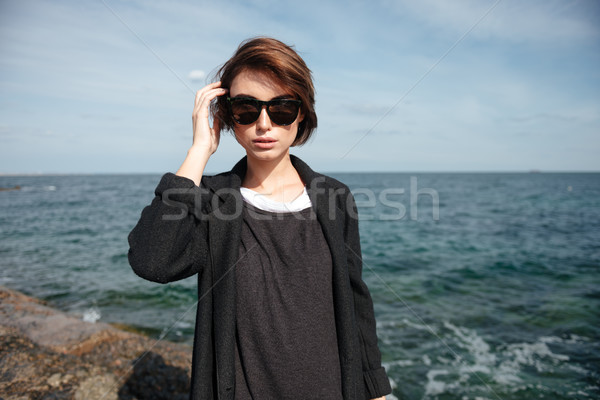 Attractive young woman in sunglasses standing on seashore Stock photo © deandrobot