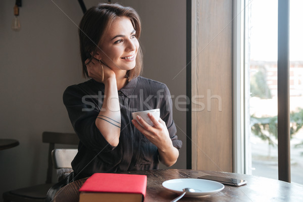 Young lady sitting at the table drinking coffee. Look aside. Stock photo © deandrobot