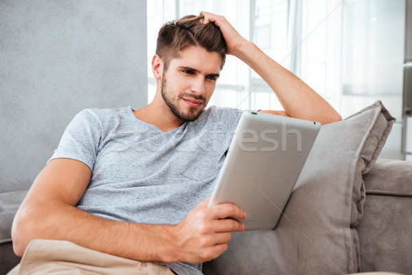 Cheerful man looking at tablet while sitting on sofa Stock photo © deandrobot