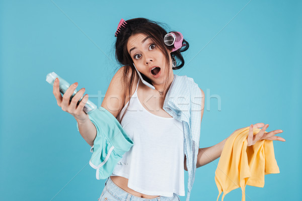Confused young woman talking by phone and holding clothes Stock photo © deandrobot