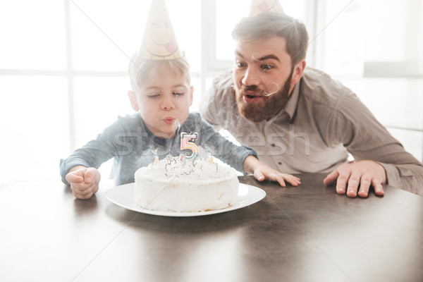 Cheerful father sitting near birtday cake with his little son. Stock photo © deandrobot