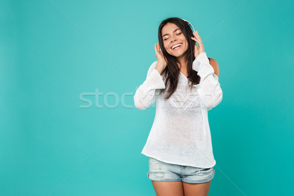 Stock photo: Cheerful young woman in headphones standing and listening to music