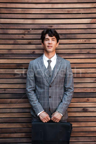 Stock photo: Handsome businessman in suit standing with briefcase against wooden wall
