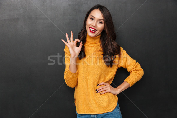 Cheerful brunette woman with arm on hip showing ok sign Stock photo © deandrobot