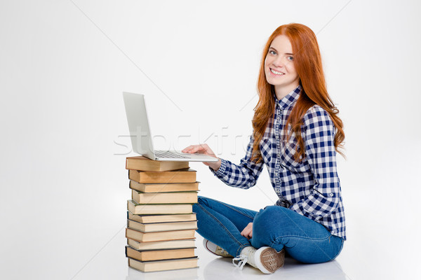 Positive female put laptop on books and using it Stock photo © deandrobot
