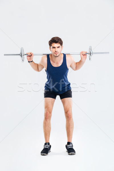 Serious young man athlete standing and exercising with barbell Stock photo © deandrobot